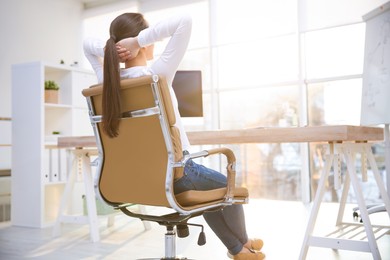 Young woman relaxing in office chair at workplace, back view