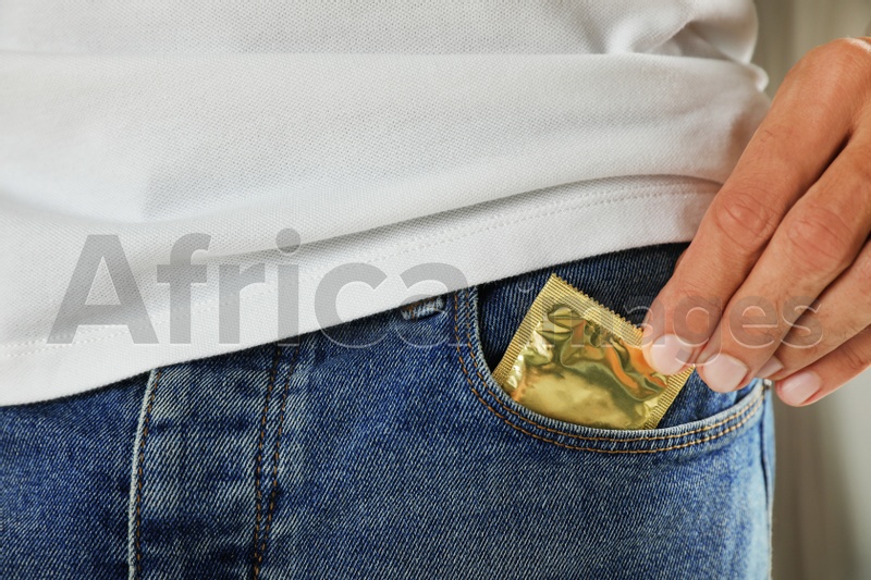 Young man pulling condom out of pocket, closeup. Safe sex concept