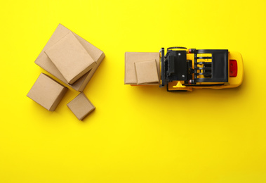 Top view of toy forklift with boxes on yellow background. Logistics and wholesale concept