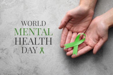 Image of World Mental Health Day. Woman holding green ribbon at grey table, top view