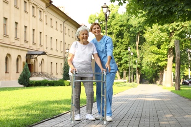Happy nurse assisting elderly woman with walking frame at park