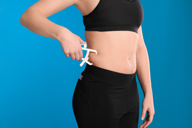 Young woman measuring body fat with caliper on blue background, closeup. Nutritionist's tool