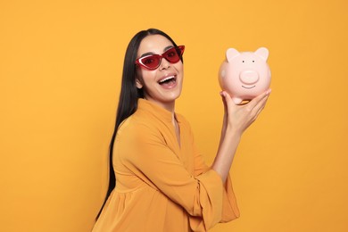 Photo of Emotional young woman with piggy bank on orange background