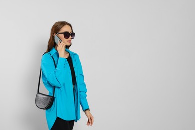 Photo of Beautiful young woman in fashionable outfit with stylish bag talking on phone against white background, space for text