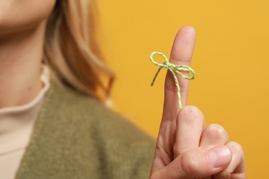 Woman showing index finger with tied bow as reminder against orange background, focus on hand