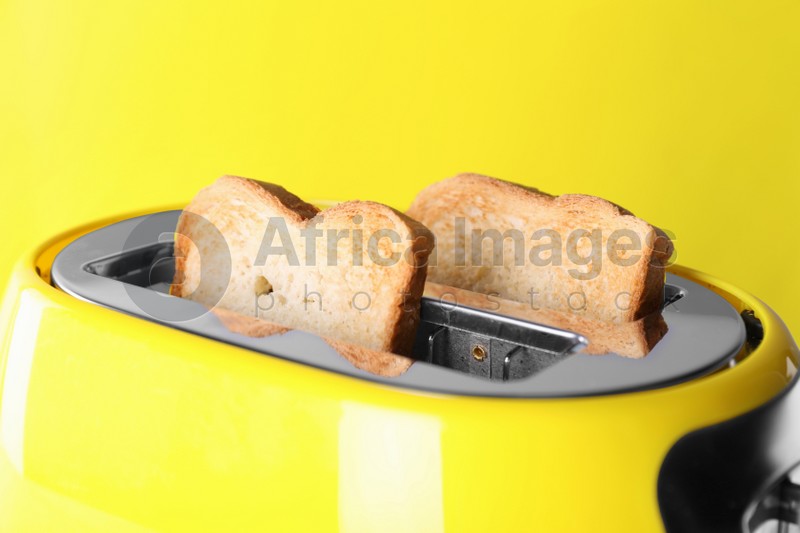 Modern toaster with slices of roasted bread against yellow background, closeup