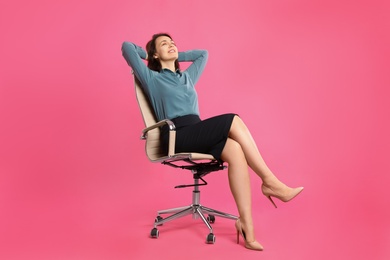 Mature businesswoman relaxing in comfortable office chair on pink background