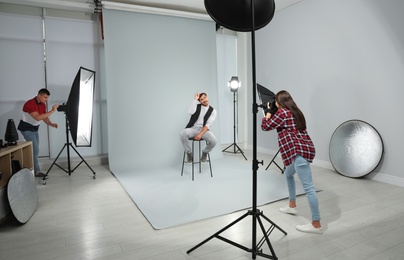Photo of Professional photographer with assistant taking picture of young man in modern studio