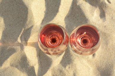 Photo of Glasses of tasty rose wine on sand, top view