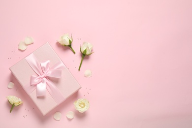 Elegant gift box and beautiful flowers on pink background, flat lay. Space for text