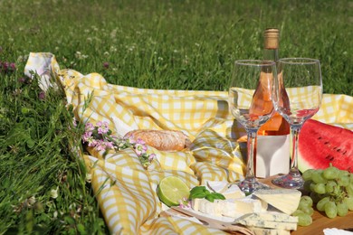 Picnic blanket with delicious food and wine on green grass outdoors, space for text
