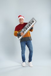Man in Santa hat playing synthesizer on light grey background. Christmas music
