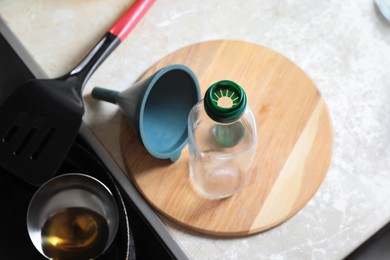 Empty bottle and funnel near frying pan with used cooking oil in kitchen