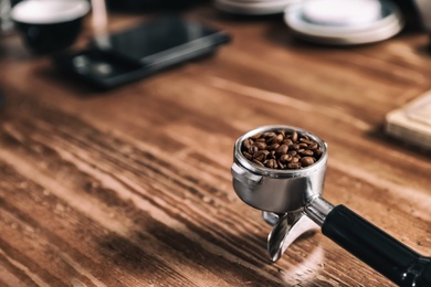 Portafilter with roasted coffee beans on wooden table. Space for text