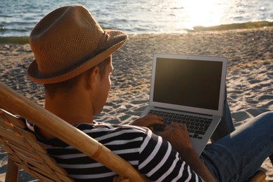 Man working with laptop in deck chair on beach