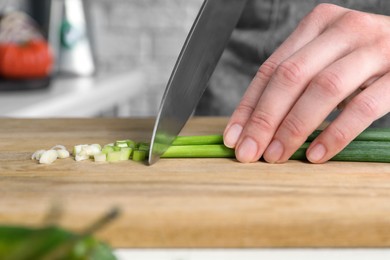 Woman cutting green spring onion on wooden board at table, closeup
