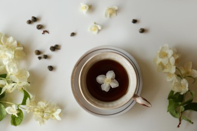 Beautiful jasmine flowers and cup of aromatic tea on white table, flat lay