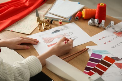 Fashion designer creating new clothes in sketchbook at wooden table, closeup