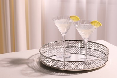 Photo of Tray with martini glasses of fresh cocktail and lemon slices on white table indoors. Space for text