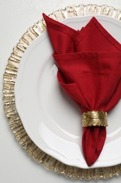 Plate with red fabric napkin and decorative ring on white table, top view