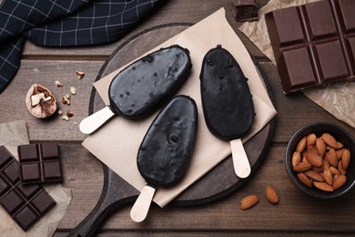 Delicious glazed ice cream bars, chocolate and nuts on wooden table, flat lay