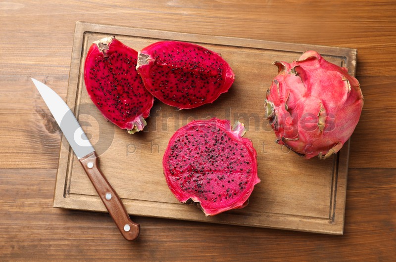 Board with delicious red pitahaya fruits and knife on wooden table, top view