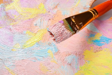Closeup view of artist's palette with mixed pastel paints and brush as background
