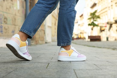 Woman in stylish sneakers walking on city street, closeup