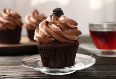 Delicious chocolate cupcake with cream and blackberry on black wooden table, closeup