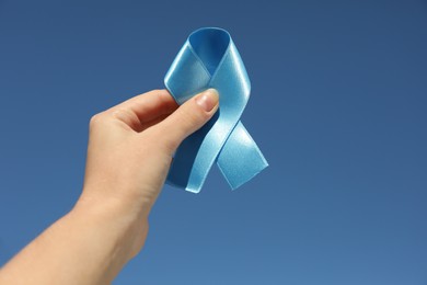 Woman holding light blue awareness ribbon against sky, closeup