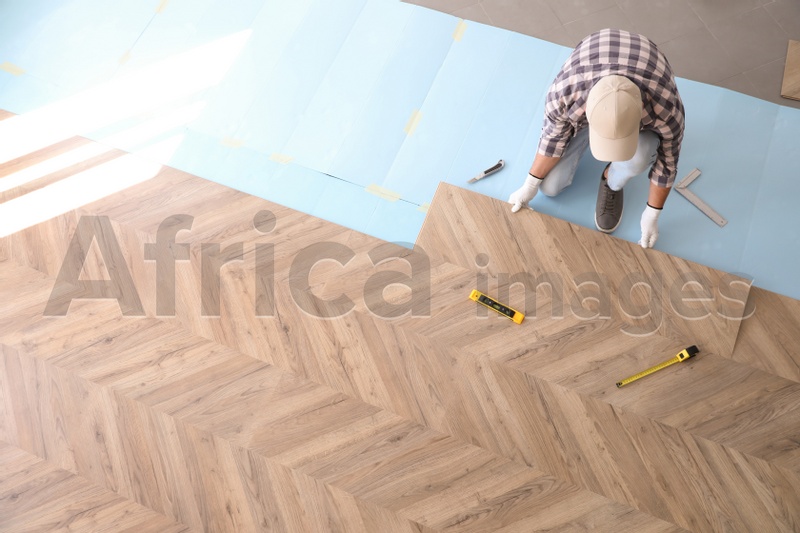 Worker installing laminated wooden floor indoors, above view