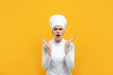 Photo of Emotional female chef wearing uniform and cap on orange background