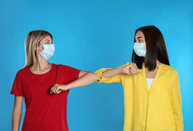 Photo of Women bumping elbows to say hello on light blue background. Keeping social distance during coronavirus pandemic