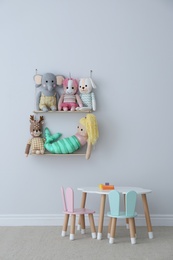Table, chairs with bunny ears and collection of cute toys in child's room interior