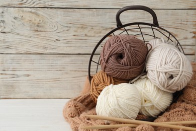 Photo of Soft woolen yarns with knitting needles and sweater on white table, closeup. Space for text