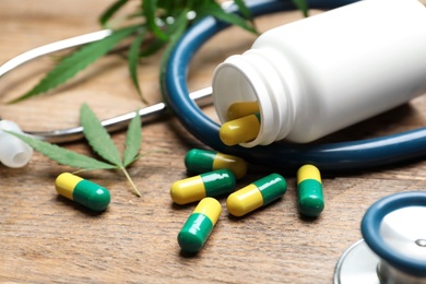 Hemp leaves, capsules and stethoscope on wooden table, closeup