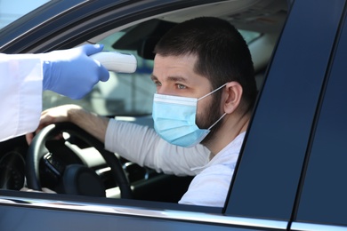 Doctor measuring driver's temperature with non contact infrared thermometer outdoors