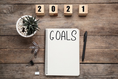 Notebook with word Goals near number 2021 made of cubes, new year aims. Objects on wooden table, flat lay