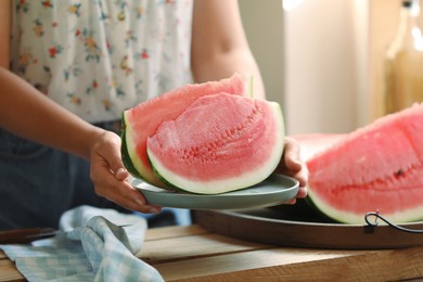 Woman holding plate with sliced fresh juicy watermelon over wooden table, closeup