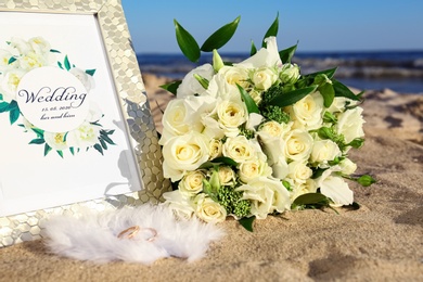 Composition with wedding invitation and gold rings on sandy beach