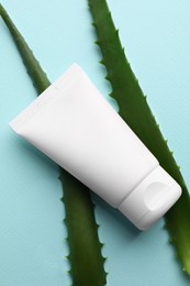 Tube of hand cream and aloe on turquoise background, flat lay