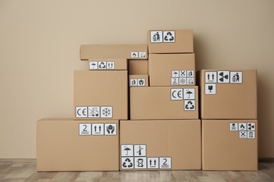 Cardboard boxes with different packaging symbols on floor near beige wall. Parcel delivery