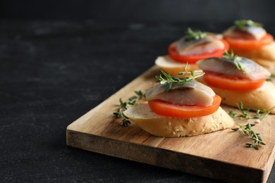 Photo of Delicious sandwiches with salted herring, tomato and thyme on black table, closeup. Space for text