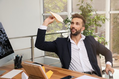 Handsome businessman playing with paper plane at desk in office