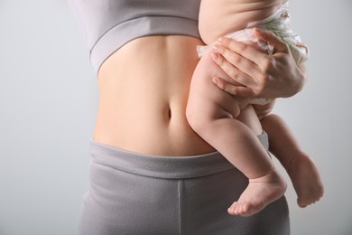 Photo of Mother with bare belly holding her baby on light grey background, closeup