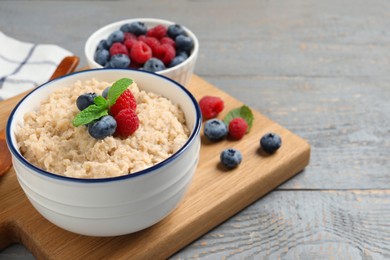 Tasty oatmeal porridge with berries on grey wooden table. Space for text