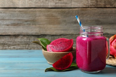 Delicious pitahaya smoothie in mason jar and fresh fruits on light blue wooden table, space for text