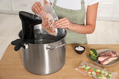 Photo of Woman putting vacuum packed meat into pot with sous vide cooker indoors, closeup. Thermal immersion circulator