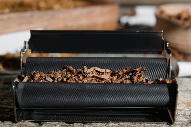 Photo of Roller with tobacco on old wooden table, closeup. Making hand rolled cigarettes