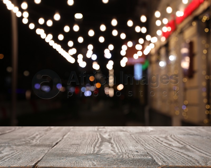 Empty wooden surface and blurred view of night street decorated for Christmas. Bokeh effect